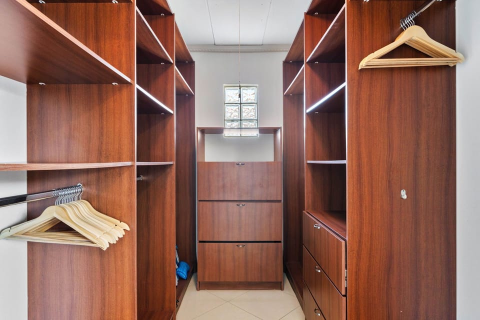 - Spacious walk-in closet with rich wooden shelving and storage space - Thoughtfully designed to keep your wardrobe organized and easily accessible - Natural light filters in, creating an inviting area for dressing and storing your essentials