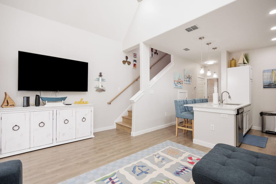 Relax in your bright, modern living space featuring a cozy coastal vibe with nautical touches and an open kitchen perfect for vacation dining.
