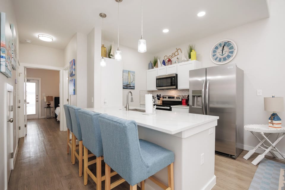 Your modern kitchen welcomes with sleek quartz counters, stainless appliances, and coastal charm throughout the bright space.