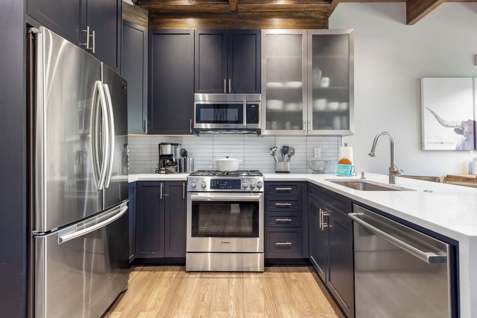 Modern kitchen with stainless steel appliances, dark cabinets, white countertops, and light wood flooring.