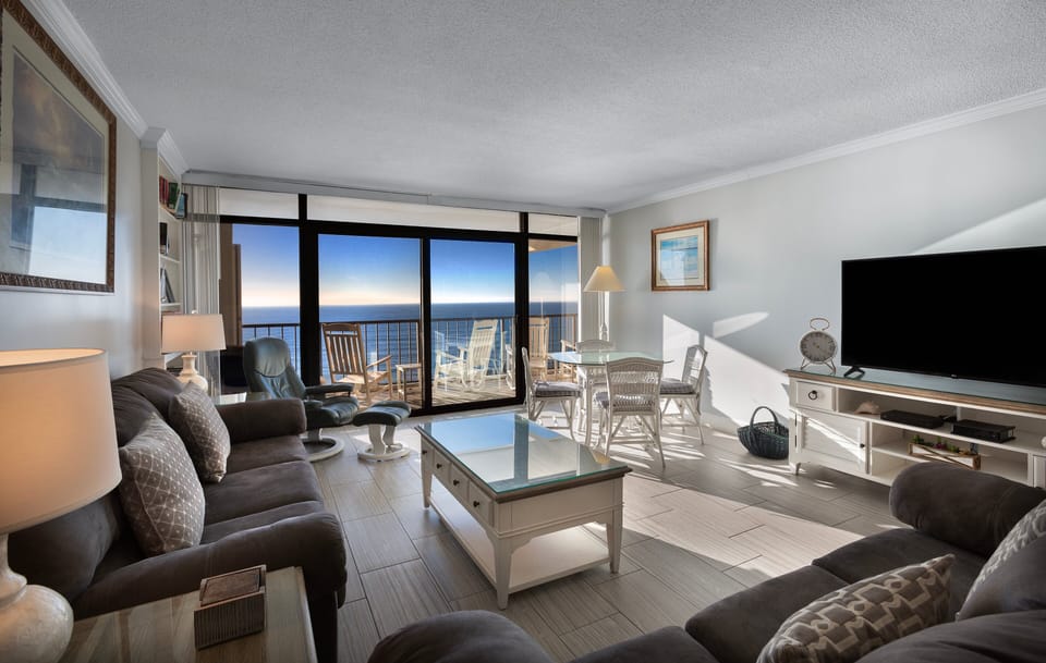 Living Room - Open living area with seating, TV, and sliding glass doors that lead directly to the oceanfront balcony.
