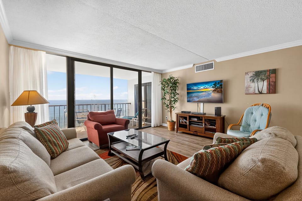 Living Room - Open living area with seating, TV, and large sliding doors leading to the oceanfront balcony.