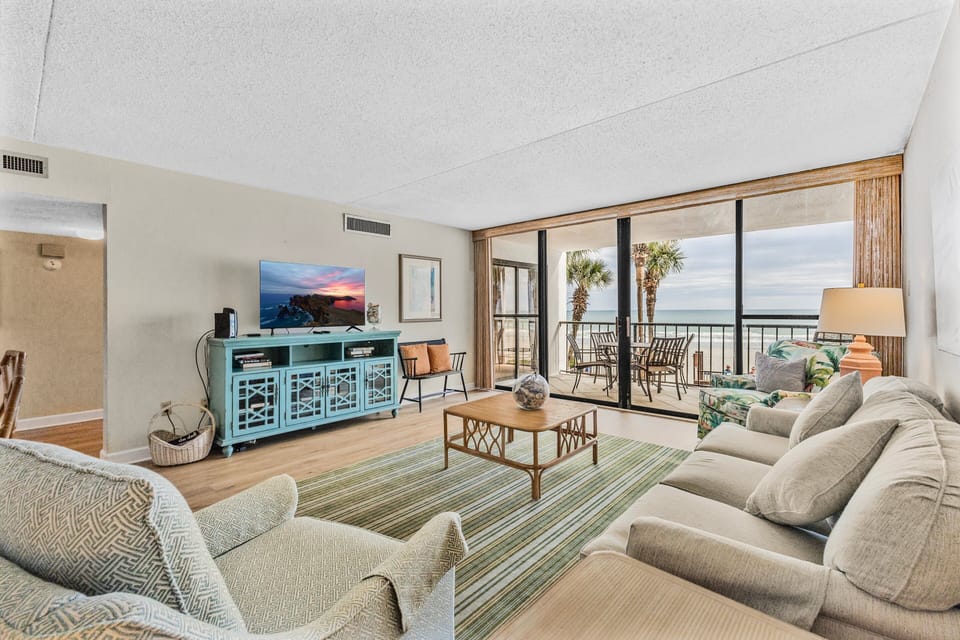 Living Room - Living area with seating, TV, and large sliding glass doors leading to the oceanfront balcony.