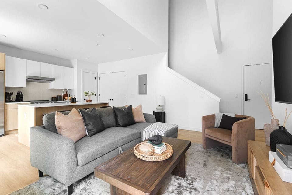 Smart TV in the living room with all the streaming apps and a comfortable sleeper sofa. Open floor plan connecting the living & kitchen areas. Natural light and high-end furnishings throughout.