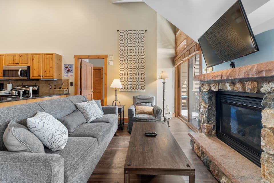 Cozy up on the plush sectional sofa by your stone fireplace, perfect for relaxing after mountain adventures with kitchen convenience nearby.