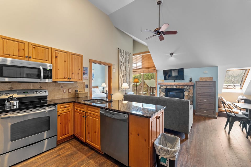 Your spacious open-concept home features a fully equipped kitchen flowing into a cozy living area with stone fireplace and mountain views.