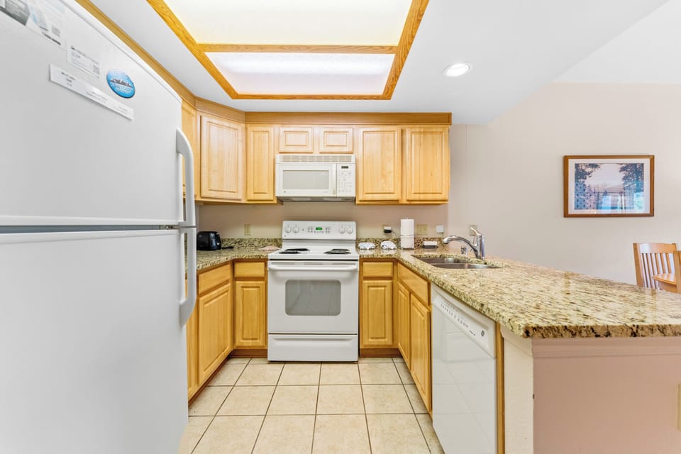 Your fully equipped kitchen features granite countertops, warm wood cabinets, and a bright skylight overhead, creating the perfect space for preparing meals.