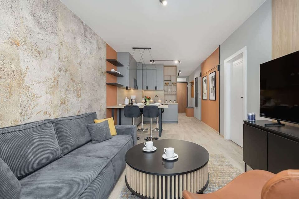 Modern living space with a gray sectional sofa, round coffee table, and kitchen area in the background.