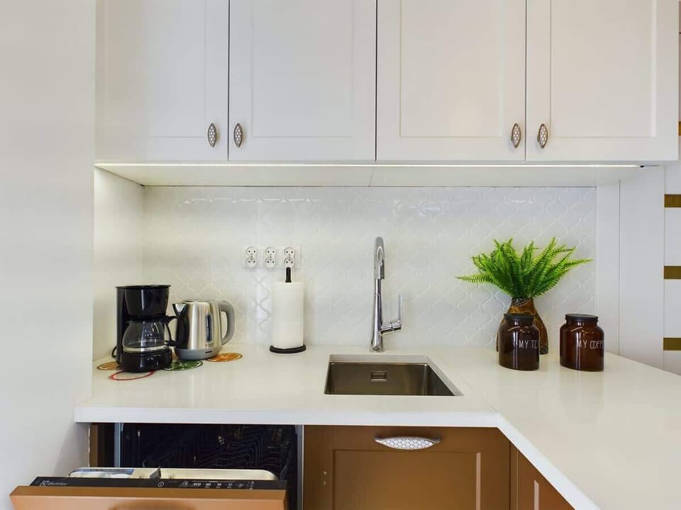 A white, minimal kitchen setup with a stovetop, coffee maker, and kettle.