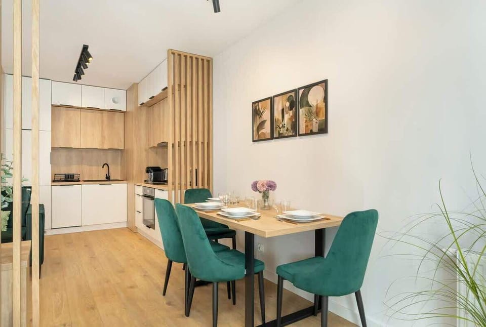 Dining table with green chairs, matching the sofa, and integrated kitchen space with white and wood cabinets.