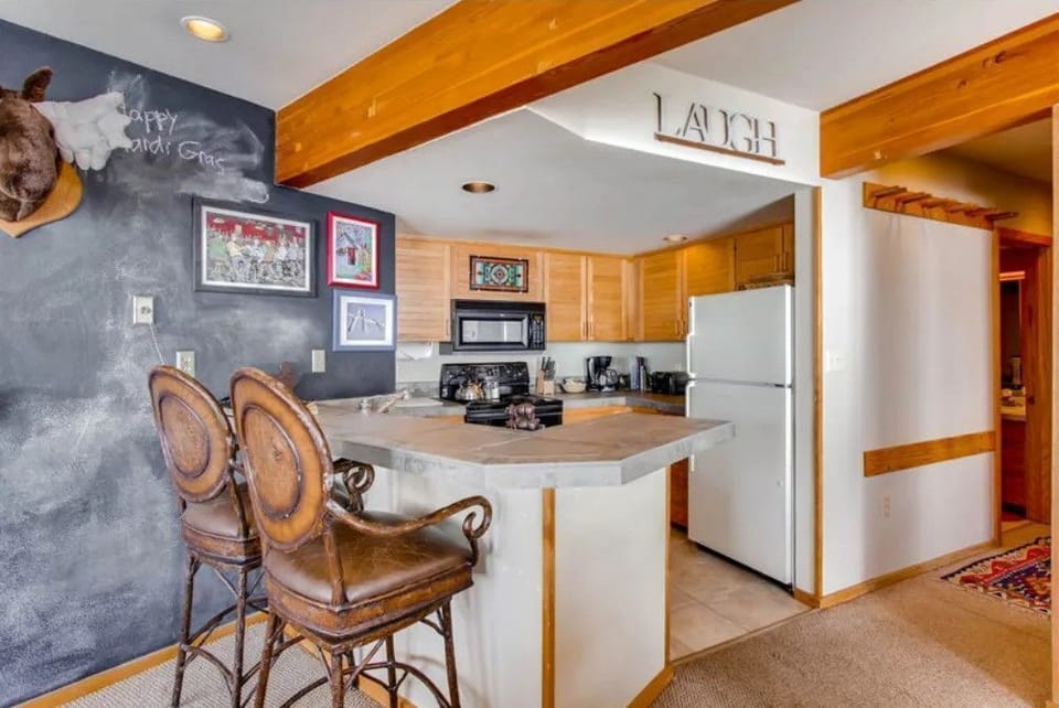 The inviting kitchen area features polished countertops and rustic decor, blending cheerful artwork with a cozy bar seating arrangement perfect for gathering.
