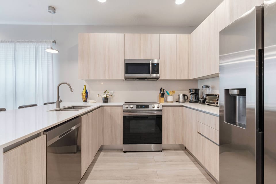 Welcome to this beautiful kitchen featuring light wood cabinetry and stainless steel appliances. The spacious countertop is perfect for meal prep, and natural light through sheer curtains creates a warm, inviting atmosphere for.