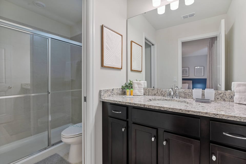 Experience the elegant bathroom with a sleek granite countertop, dark cabinetry for sophistication, and bright lighting that enhances the space. Enjoy a refreshing escape in the glass-enclosed shower for a perfect retreat.