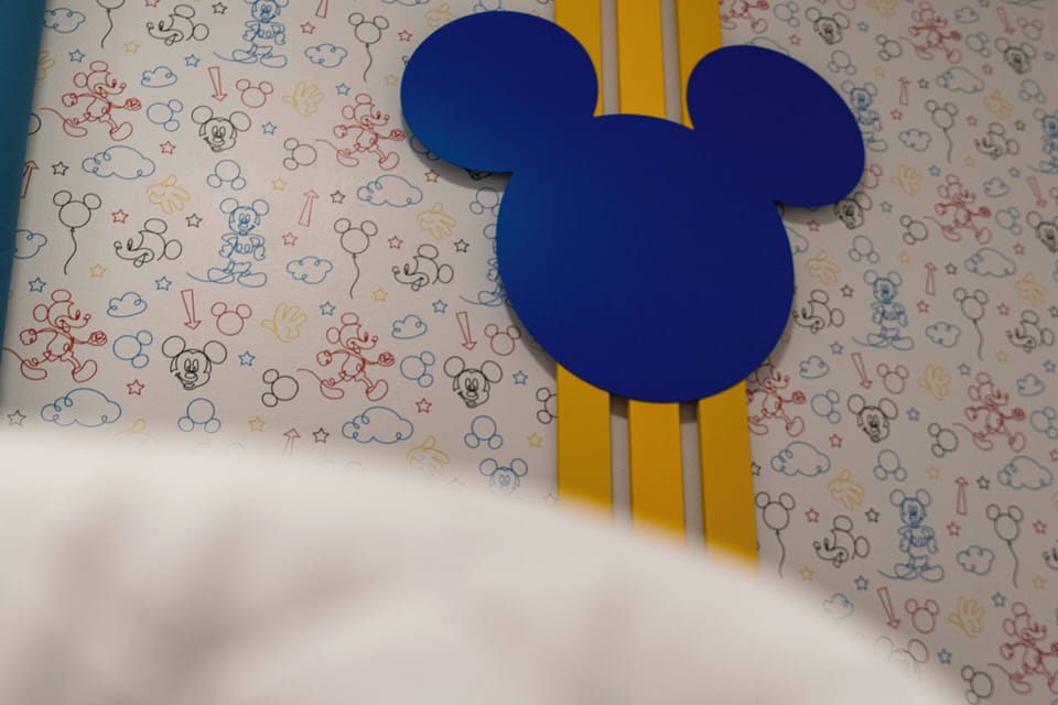 Bright and playful, this room features a whimsical blue Mickey Mouse accent against a colorful, cartoon-patterned wallpaper. The vibrant design invites fun and creativity, making it a delightful space for guests of all ages.