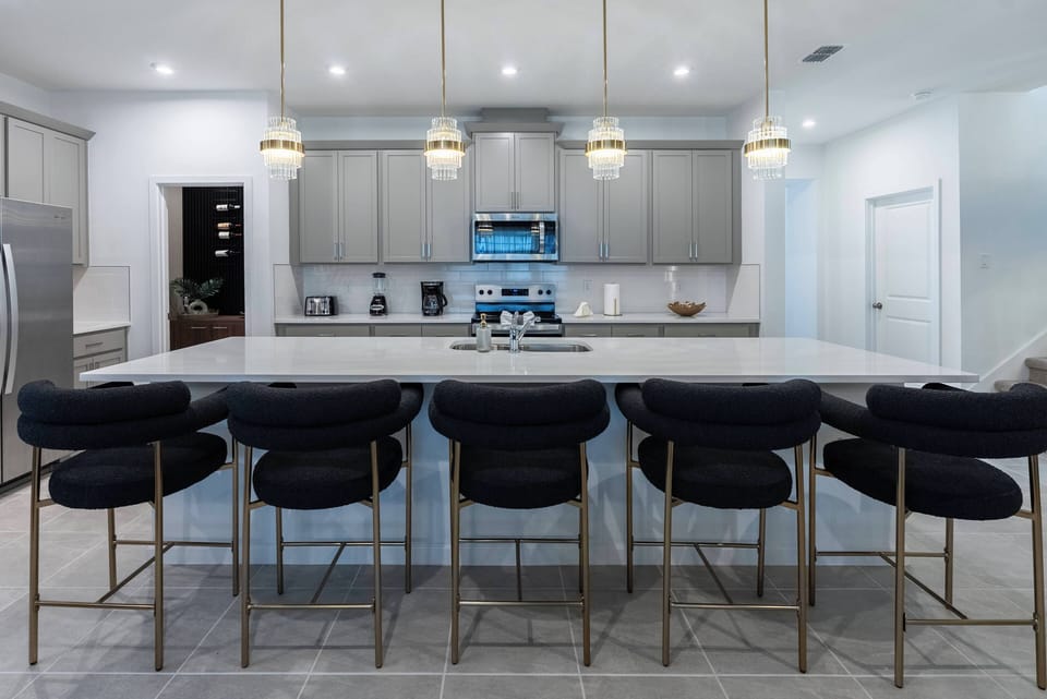 This stylish kitchen boasts a spacious island with elegant gold-accented seating, ideal for casual meals or morning coffee. With sleek cabinetry and modern appliances, it's a bright and functional space that inspires culinary.