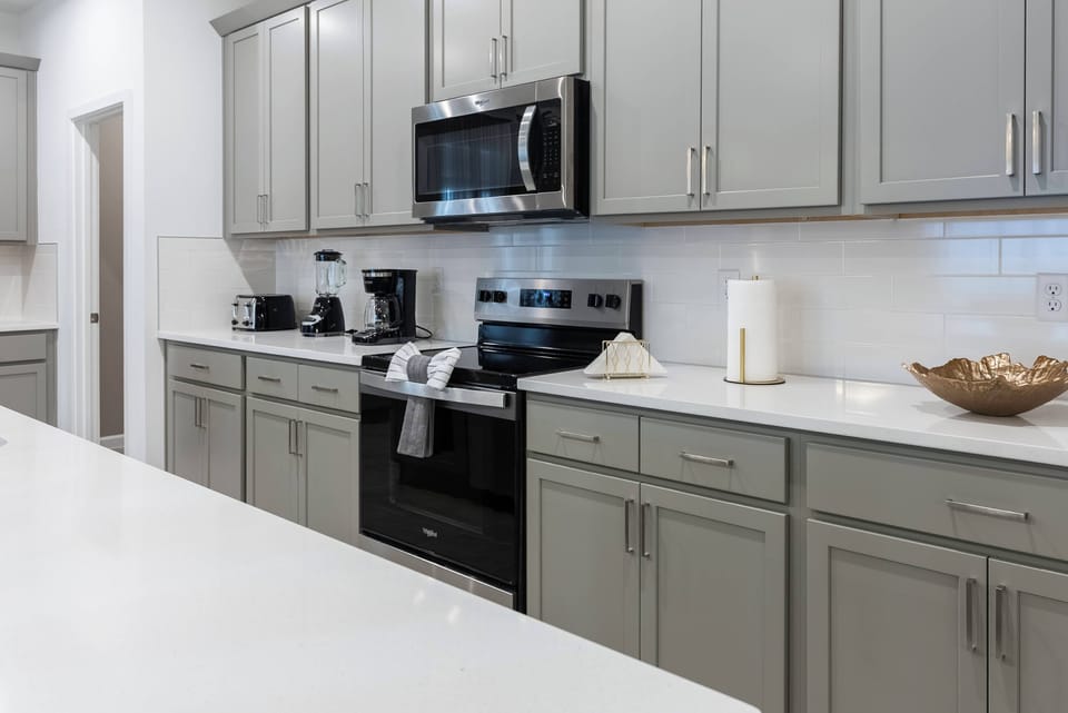 Welcome to a stylish kitchen featuring sleek gray cabinets and a bright white countertop. Enjoy modern appliances, including a black stove and microwave, all complemented by a decorative bowl that adds a cozy, homey touch.