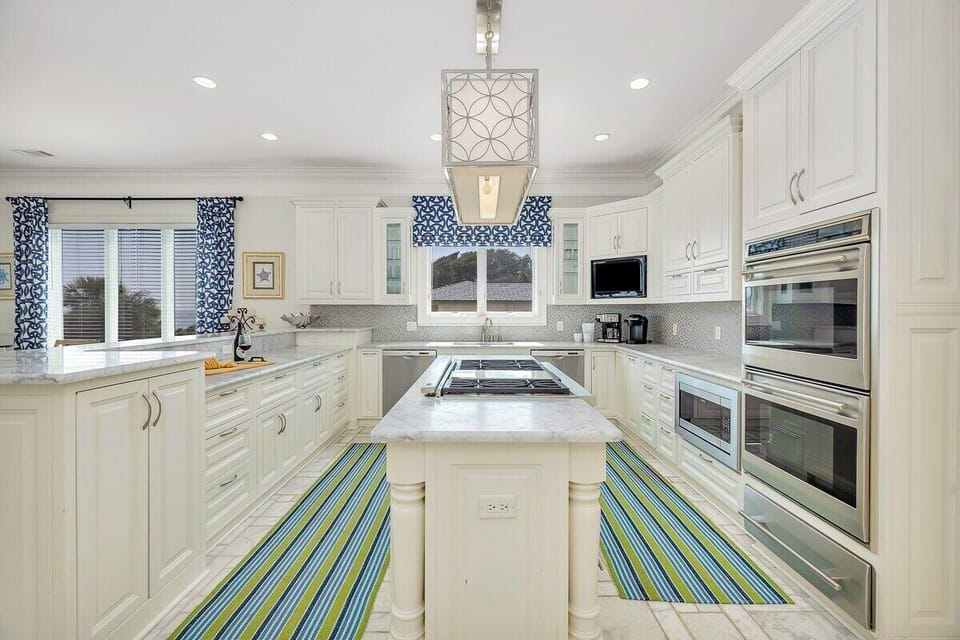White kitchen with long island, teal stools, and pendant