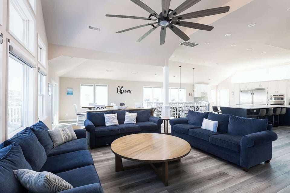 Spacious top-level living area featuring a large flat-screen TV and expansive windows with neighborhood views and a glimpse of the ocean