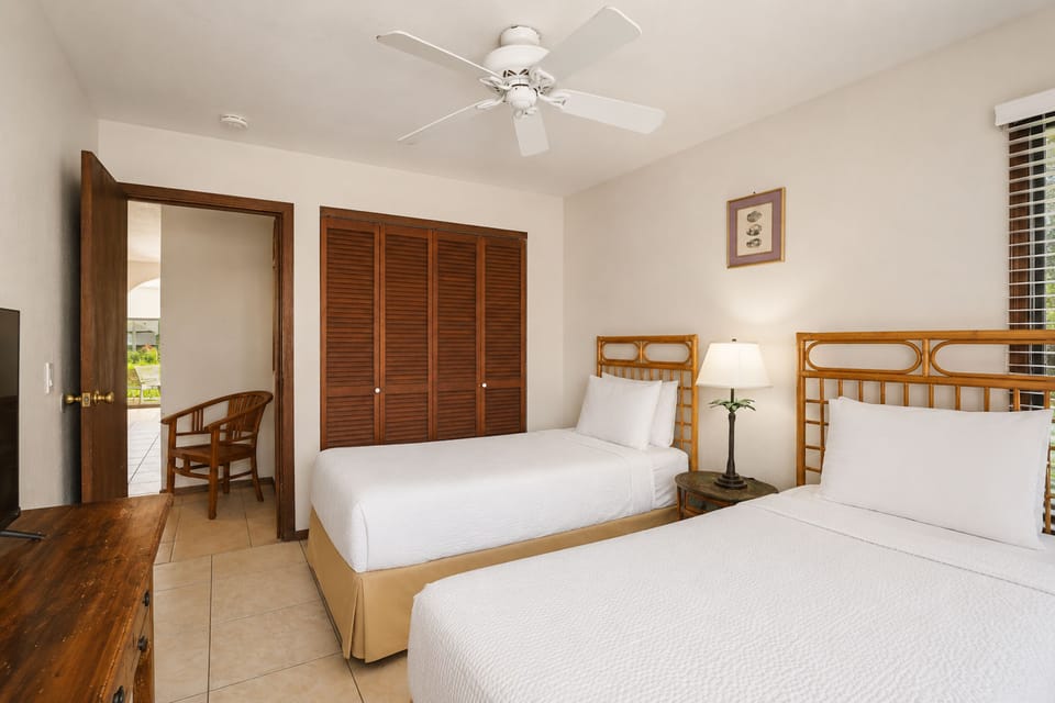 Your bright tropical retreat features two comfortable beds, bamboo-inspired frames, and breezy ceiling fan keeping you cool. Warm wood tones and crisp white linens create a serene island escape.