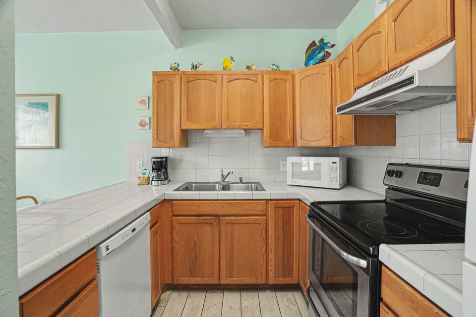 Your fully-equipped kitchen awaits with warm wood cabinetry, modern appliances, and cheerful coastal décor—perfect for preparing your favorite meals after a day at the beach.
