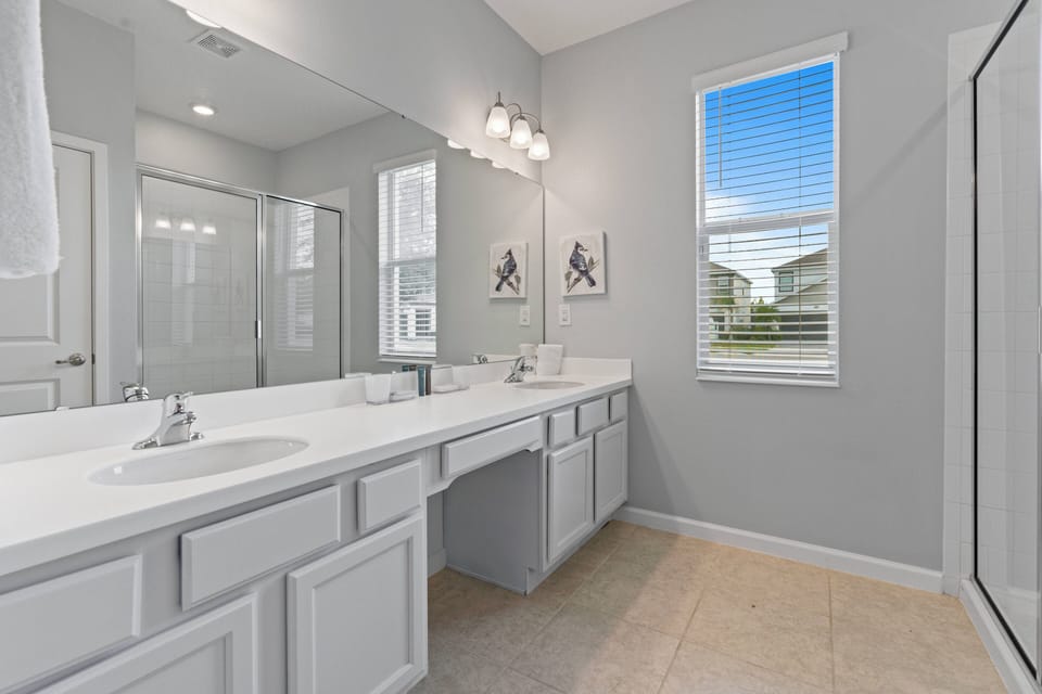 Enjoy a bright and airy bathroom featuring a spacious dual vanity, sleek white cabinetry, and a large mirror that floods the space with natural light. Relax in the glass-enclosed shower with elegant fixtures for ultimate comfort.