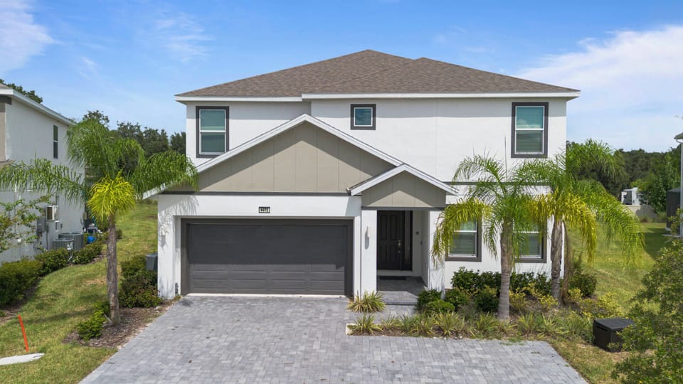 This striking home features a welcoming facade with clean lines and light-colored walls, complemented by a charming porch and lush greenery. The spacious driveway adds to the appeal, making arrivals feel special and effortless.