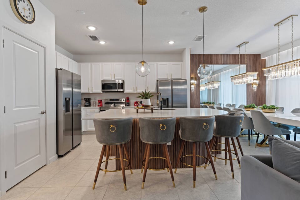 Welcome to this stylish kitchen with sleek white cabinetry and modern fixtures for a bright atmosphere. Enjoy your morning coffee at the spacious island, complete with cozy gray bar stools and warm, inviting lighting.