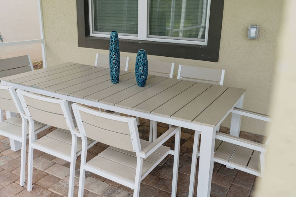 Enjoy the charm of al fresco dining at our spacious outdoor table, designed with a sleek white finish that harmonizes with the patio's earthy tones. Colorful vases enhance the ambiance, making it perfect for gatherings.