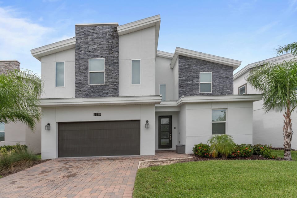This stunning vacation home features a chic facade with a mix of sleek white stucco and textured stone, creating an appealing contrast. Large windows fill the space with natural light, while the manicured landscaping adds charm.
