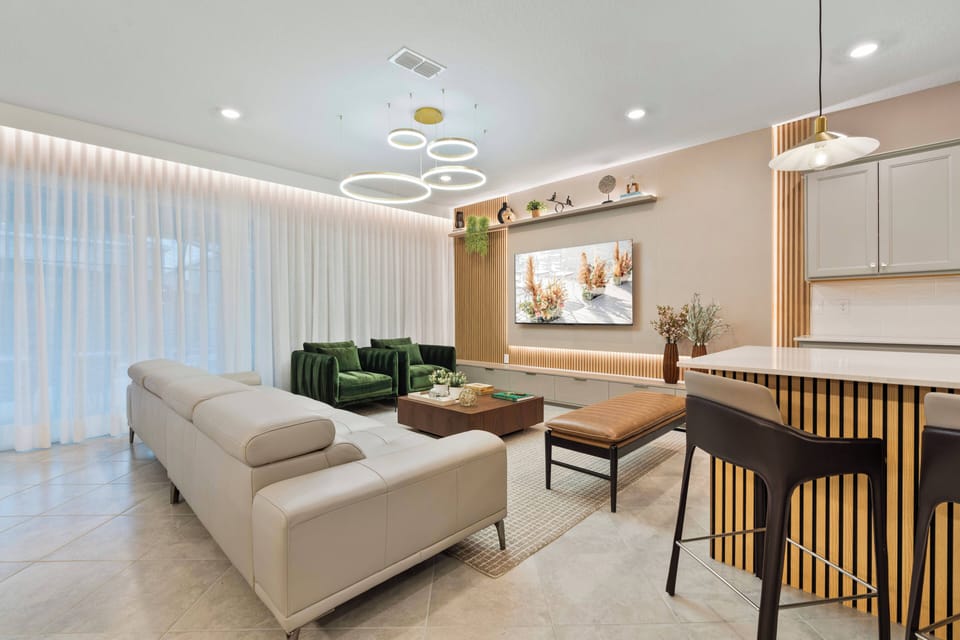 Enjoy a bright living area with a stylish mix of textures, from the soft cream sofa to rich green armchairs, all illuminated by large windows and modern light fixtures for a sophisticated atmosphere.