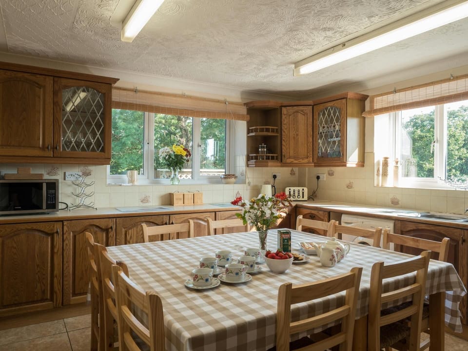 Kitchen cupboards, microwave, toaster, kettle, washing machine, sink, dining table with 10 chairs and two large windows