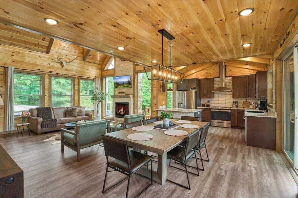 Spacious open-concept living with a dining table for six plus three additional seats at the kitchen island. Enjoy a cozy fireplace, modern kitchen, and large windows with serene views. Perfect for family gatherings and relaxing mountain getaways!