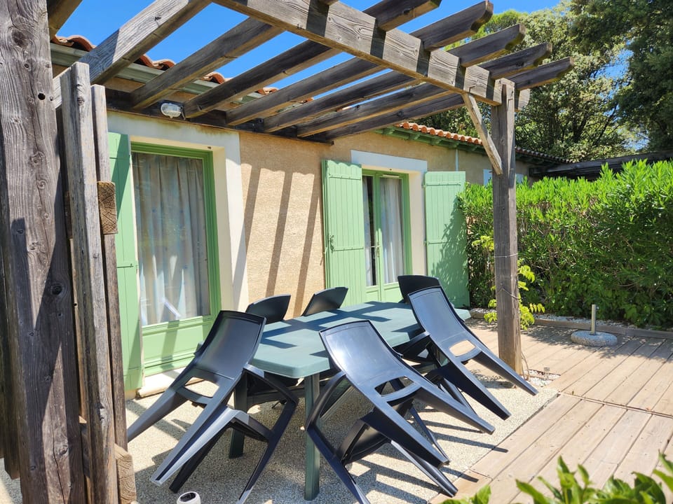 Stacked black chairs sit beside the patio table, framed by green shutters and the pergola overhead.