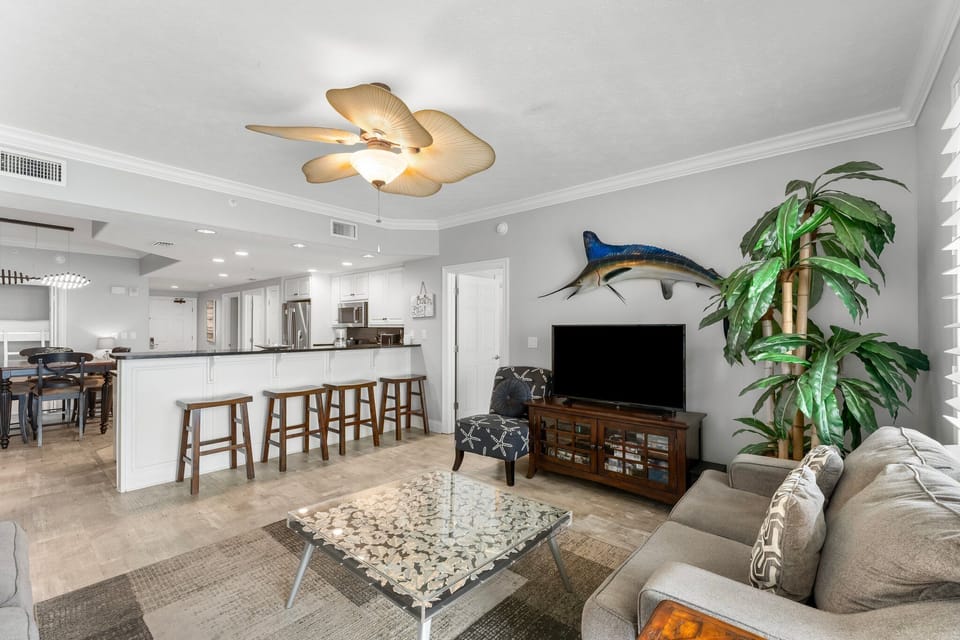 Open living area with a coastal-themed ceiling fan and bar seating.