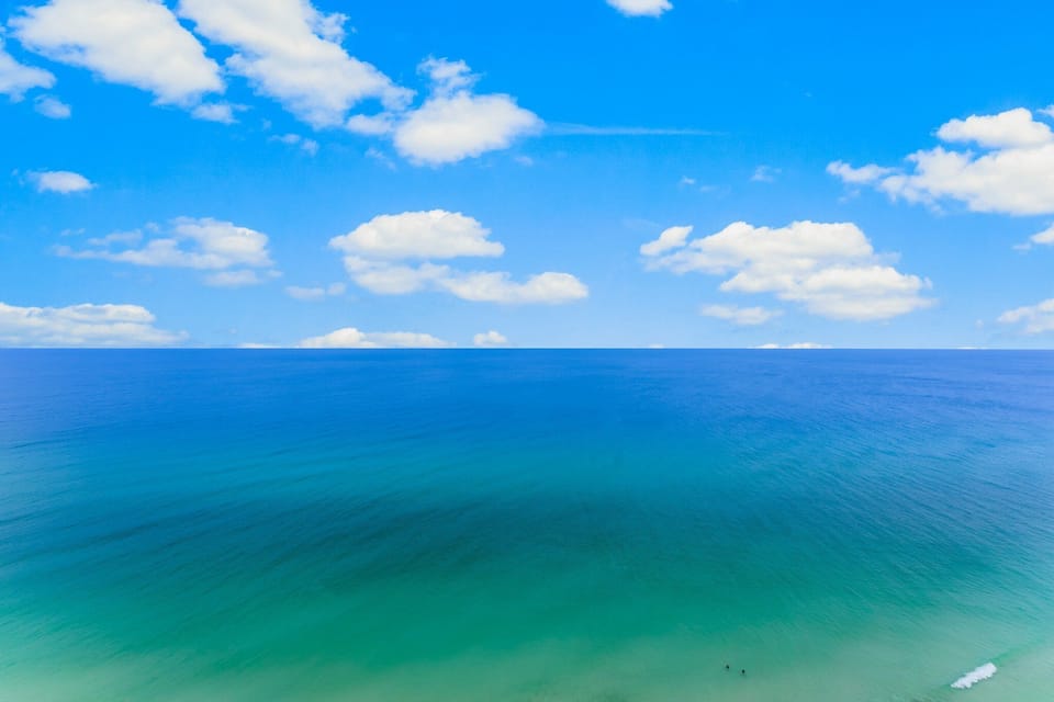 Clear ocean view under a bright blue sky with scattered clouds