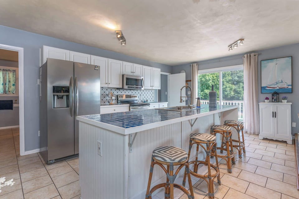 Stunning updated kitchen with large island and peninsula countertop, bar seating, stainless steel appliances, modern cabinetry, tile backsplash, and ample prep space