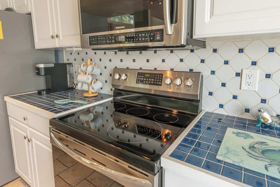 Stunning updated kitchen with large island and peninsula countertop, bar seating, stainless steel refrigerator, stove, oven, microwave , coffee maker, modern cabinetry, tile backsplash, and ample prep space