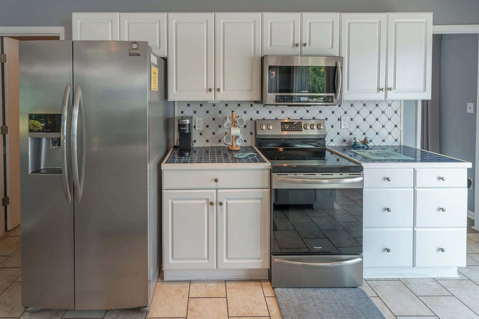 Stunning updated kitchen with large island and peninsula countertop, bar seating, stainless steel refrigerator, stove, oven, microwave , coffee maker, modern cabinetry, tile backsplash, and ample prep space