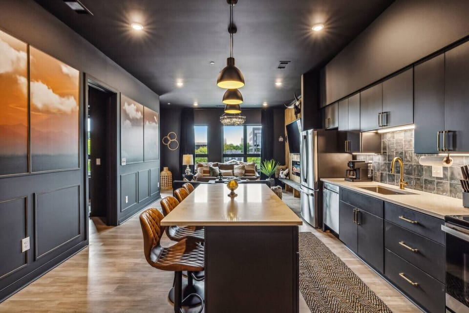 Modern and stylish open-concept kitchen and living area. The kitchen features dark cabinets, a sleek white countertop, and contemporary bar stools.