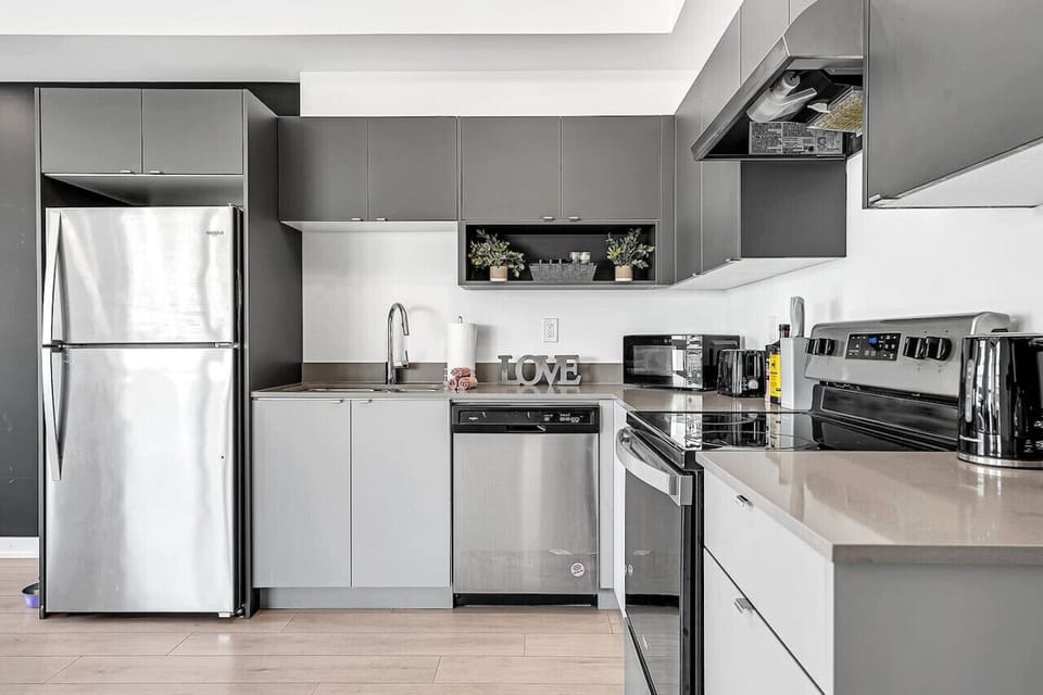 Calling all home chefs! This fully equipped, modern kitchen features high-end stainless steel appliances, including a full-sized fridge, dishwasher, and electric range. The sleek grey cabinetry is stocked with all the essentials you need to whip up a gour
