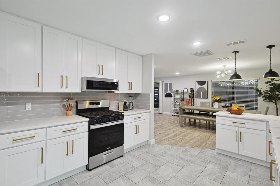 A spacious and modern kitchen with sleek white cabinetry, gold accents, and stainless steel appliances. The open design flows into the dining area, making it perfect for cooking, entertaining, and gathering with loved ones.