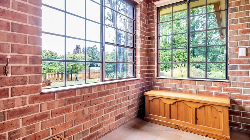This cozy sunroom features exposed brick walls and large sliding windows with classic dark frames.