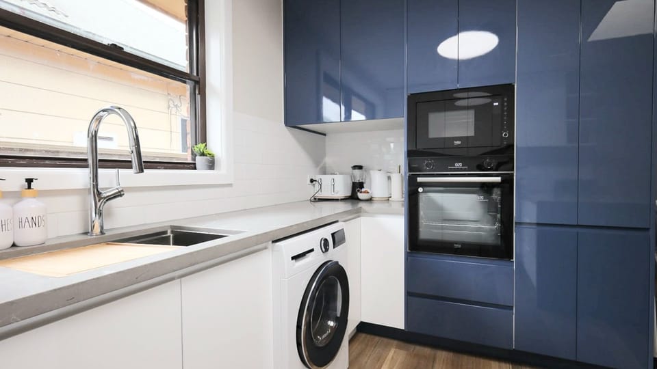 Beautifully streamlined design. From the glossy cabinetry to the seamless integration of laundry and cooking essentials, this space is the perfect example of modern, multi-purpose living.