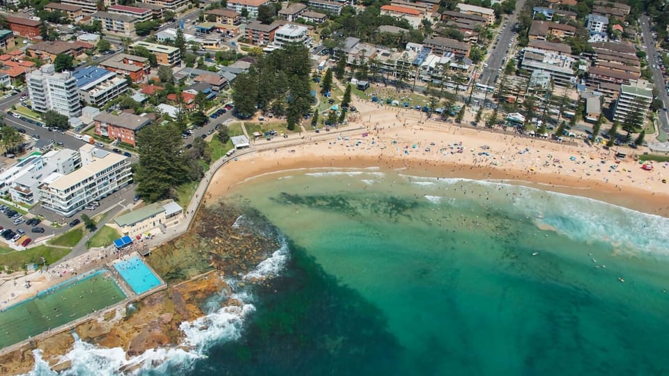 A coastal paradise from above. Take in the spectacular bird's-eye view of a vibrant, golden sand beach curving alongside crystal-clear turquoise waters and a bustling seaside town.