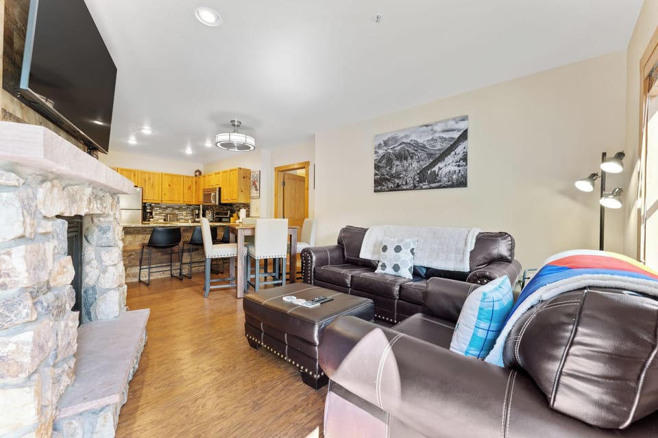 Relax in your spacious living room with leather seating, stone fireplace, and open kitchen—perfect for unwinding after mountain adventures.