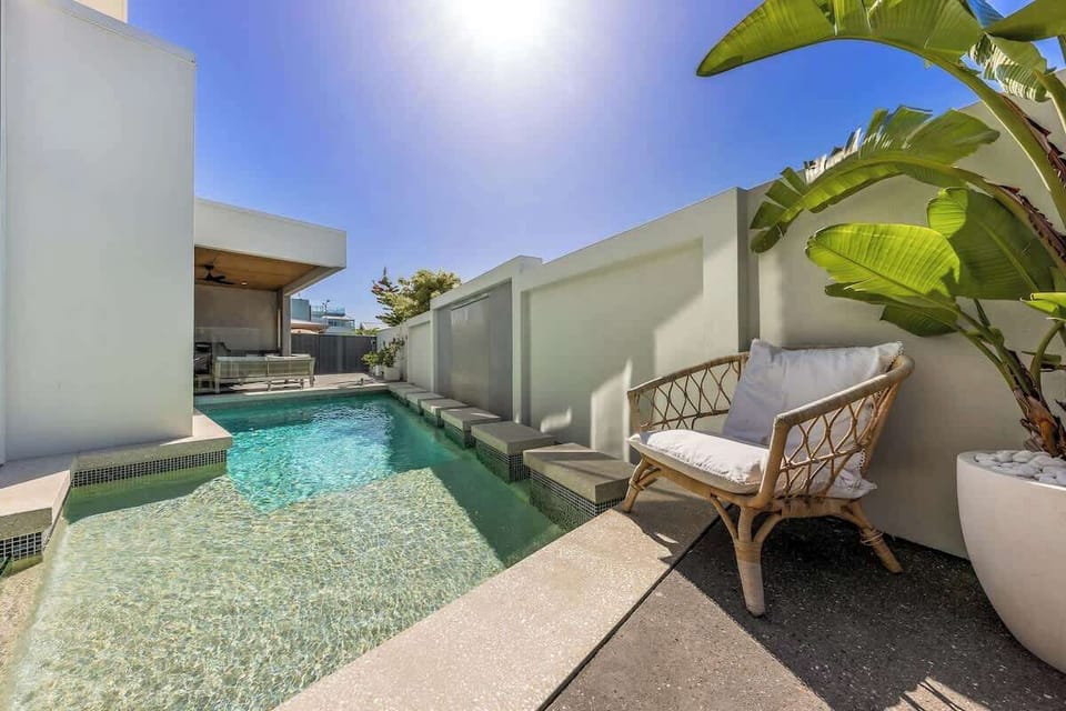  Inviting outdoor space features a beautiful swimming pool with stepping stones, a comfortable wicker chair, and lush greenery, perfect for relaxing under the sun.







