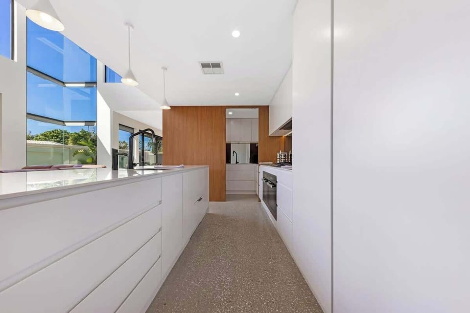  Modern kitchen features a sleek white island, stylish wooden accents, and expansive windows that let in natural light, making it a bright and inviting space for cooking and socializing.













