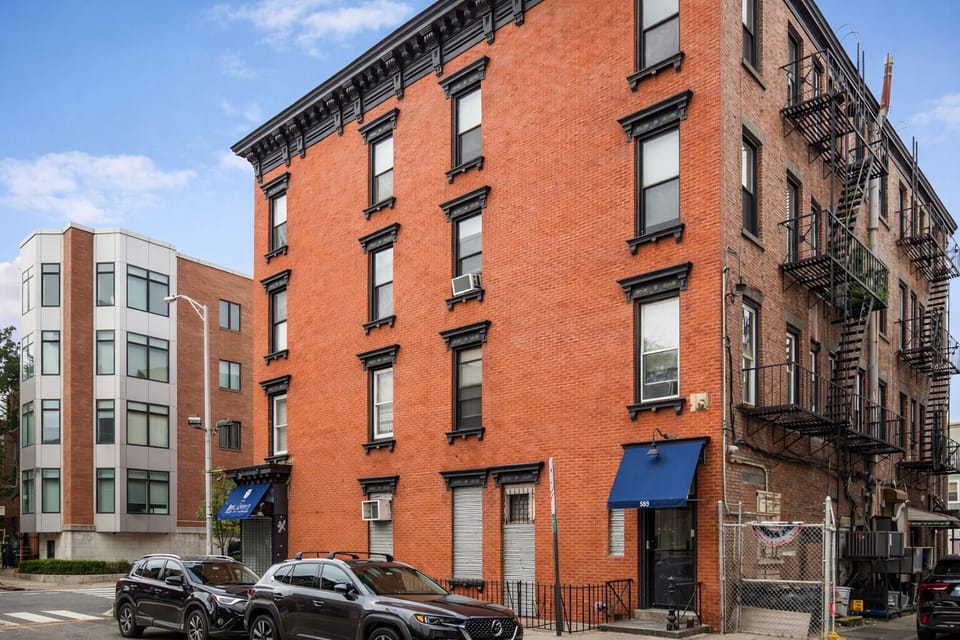 Classic red-brick corner building with fire escapes in a lively, walkable area