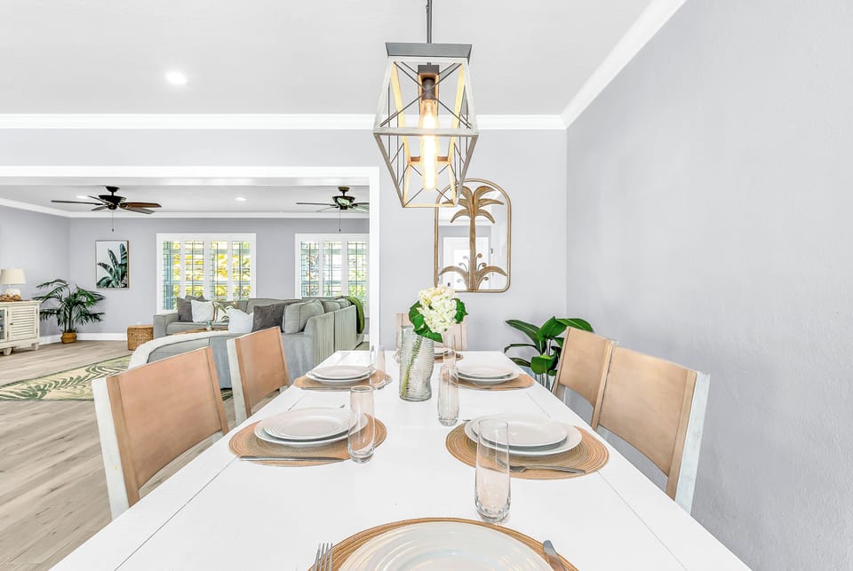 The dining area comfortably seats six beneath a farmhouse chandelier, with four additional rattan counter stools at the kitchen counter. The open floor plan allows for easy serving from the ki
