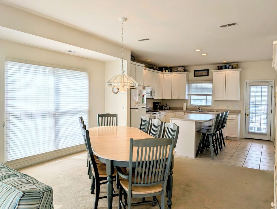 10 Dune Road (39544) - Dining Room - A bright dining space featuring a large wooden table and chairs, situated next to expansive windows that flood the room with natural light. Perfect for hosting family meals.